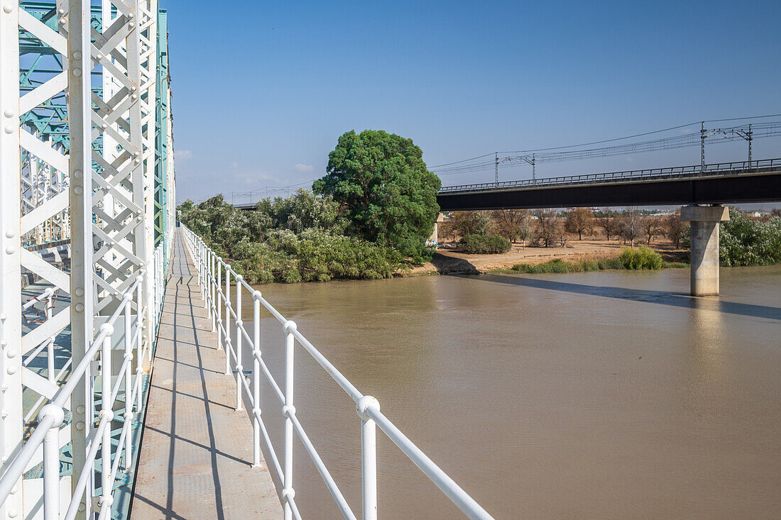 Blick auf die 1930 erbaute Eisenbrücke San Juan,die den Fluss Guadalquivir in Sevilla,Spanien,überspannt,mit einer modernen Eisenbahnbrücke im Hintergrund.