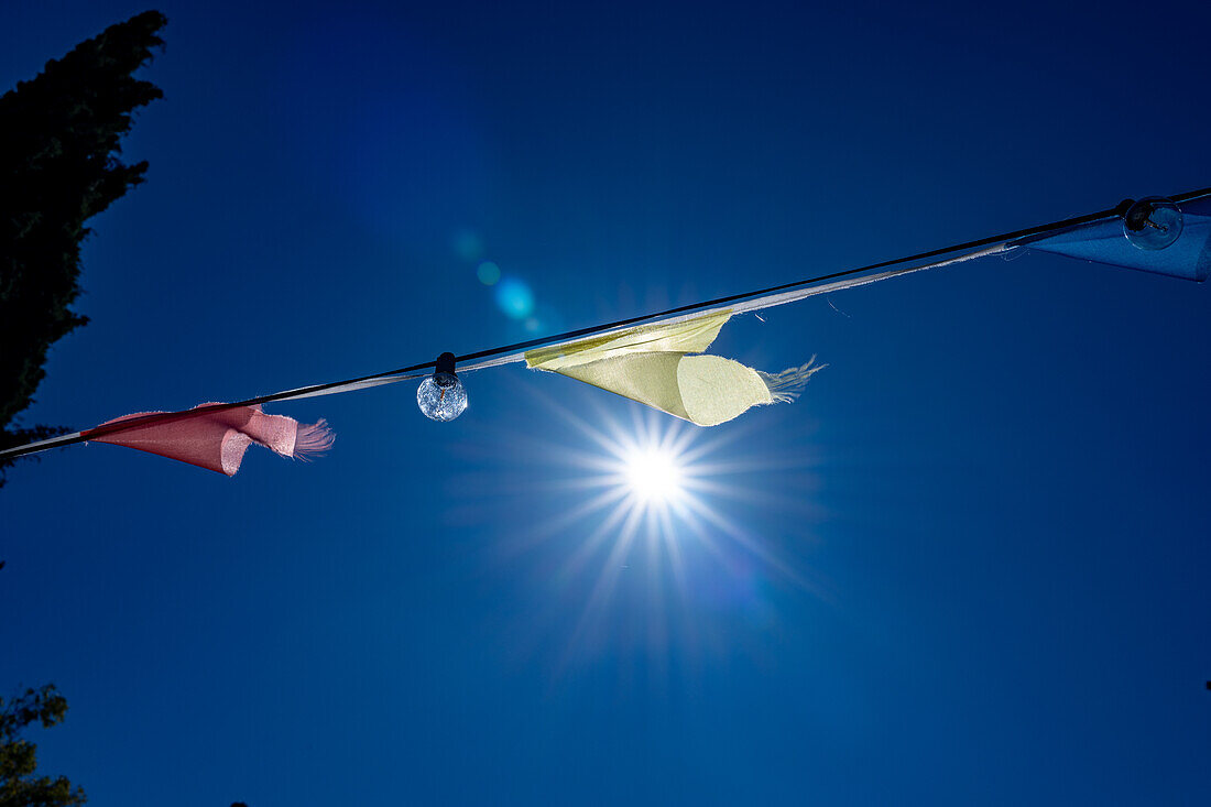 Brightly colored flags fluttering under the clear blue sky at a wedding celebration in Malaga, Spain. The sun shines brightly, creating a festive and joyful atmosphere.