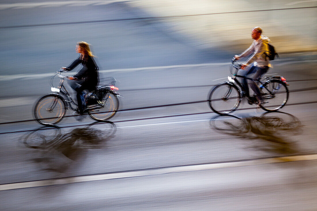 Dynamic panning photo capturing two cyclists riding through a city at night, creating a sense of speed and movement.