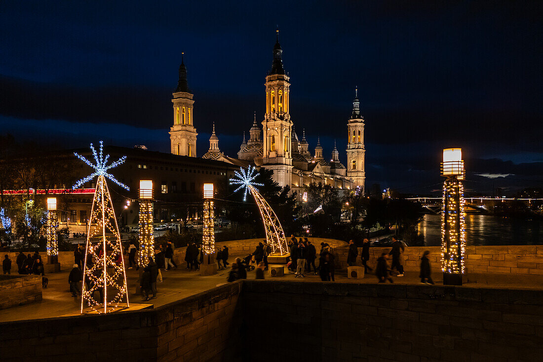 Aerial view of the Cathedral Basilica of Our Lady of the Pillar and Stone Bridge illuminated at night during Christmas, Zaragoza, Spain