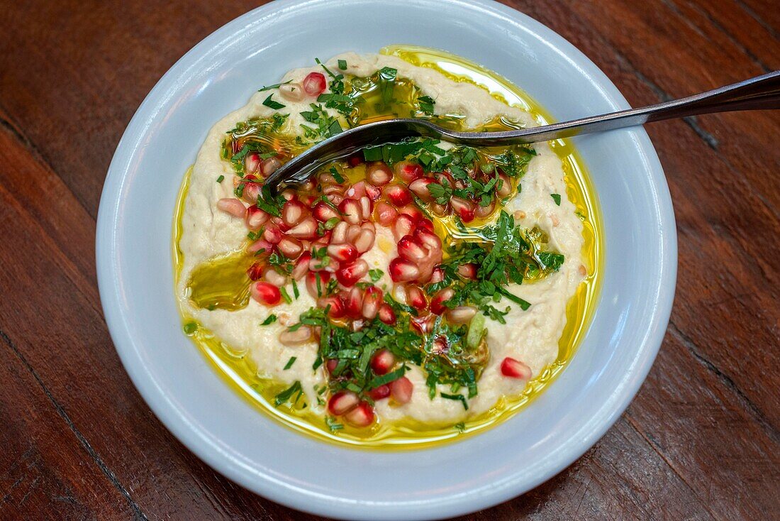 Pomegranate wirh Hummus dish. Closeup view. Arabic, vegetarian healthy food, snack or appetizer. Zajal restaurant Al Balad Steps, off Prince Muhammad Street, Al Rjoum, Amman, Jordan, Middle East. Umbrella street.