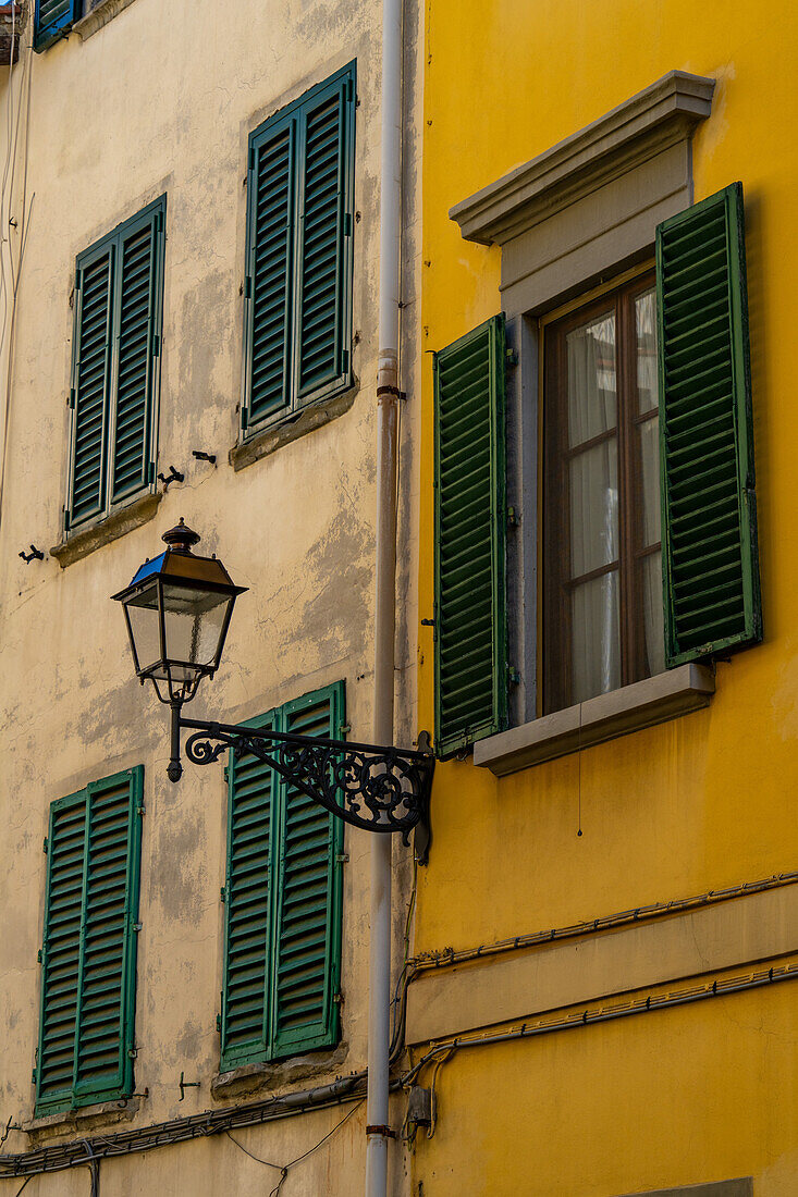 Wooden shutters and a street lamp on the colorful stucco wall of a building in historic Florence, Italy.