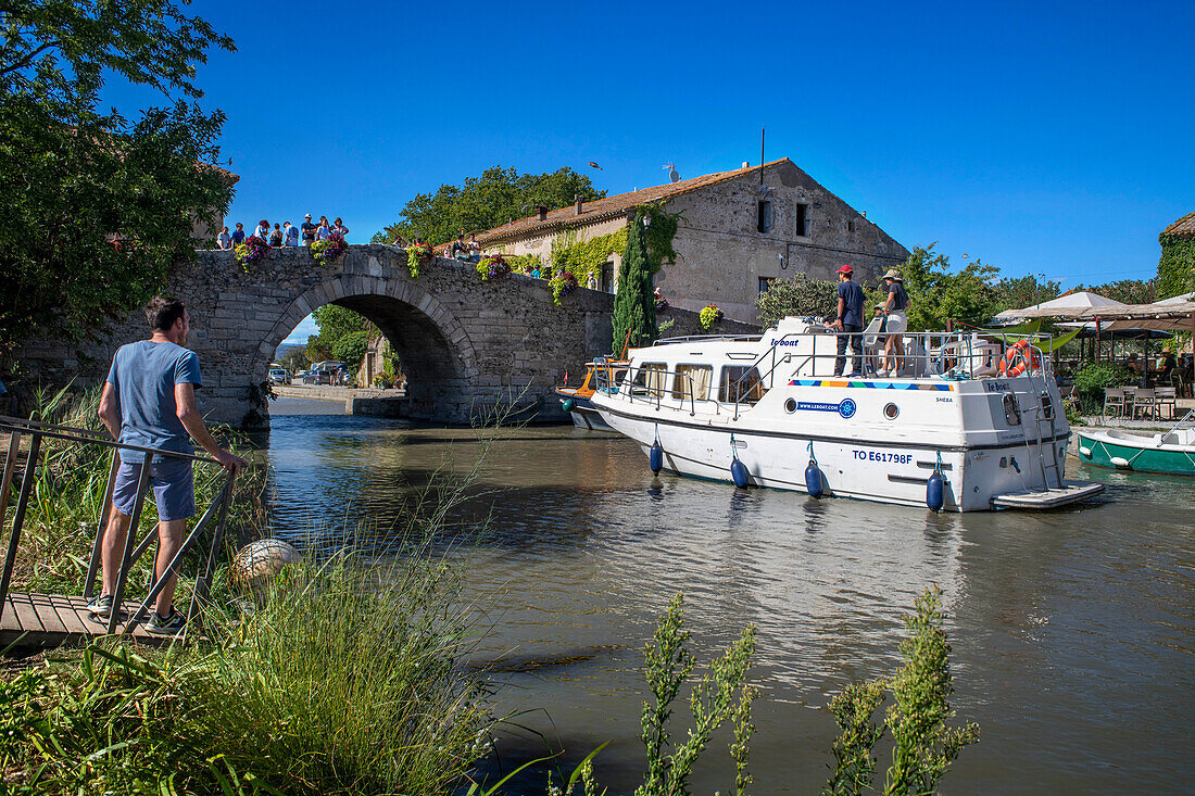 Canal du Midi an Brücke und Dorf Le Somail Aude Südfrankreich Südliche Wasserstraße Wasserstraßen Urlauber stehen Schlange für eine Bootsfahrt auf dem Fluss, Frankreich, Europa