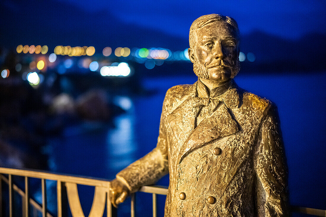 Bronze statue of King Alfonso XII on the Balcon de Europa with evening lights.