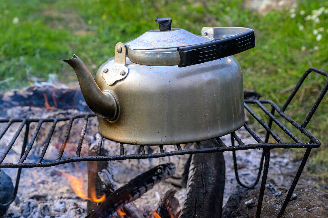 Kettle placed on a grill over a campfire, representing outdoor cooking in nature.