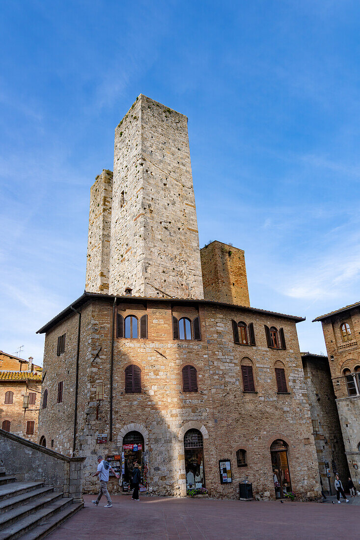 Touristen auf der Piazza del Duomo mit ihren Türmen in der mittelalterlichen Festungsstadt San Gimignano, Italien. L-R: Torri Salvucci und Torre Pettini.