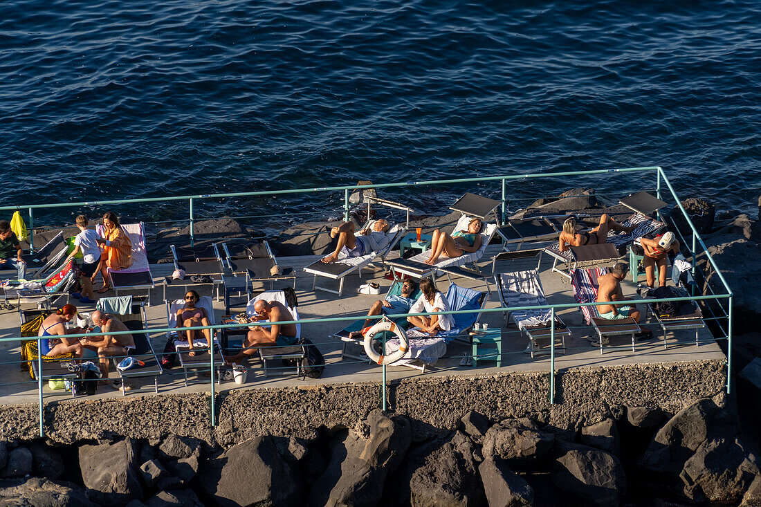 Tourists sunbathing on a recreation pier in the Bay of Naples at Sorrento, Italy.