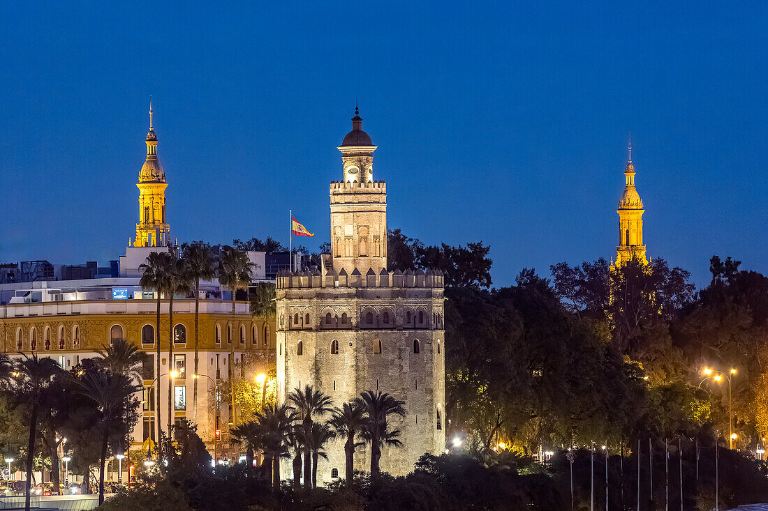 Night view of Seville landmarks including Torre del Oro and illuminated Plaza de Espana towers