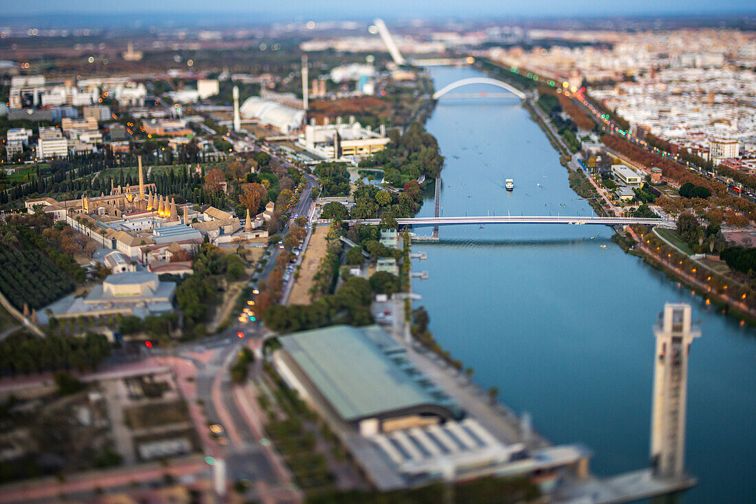 Der schillernde Sonnenuntergang beleuchtet die Isla de la Cartuja in Sevilla und hebt den Fluss und die umliegenden Gebäude mit einem Tilt-Shift-Effekt hervor.