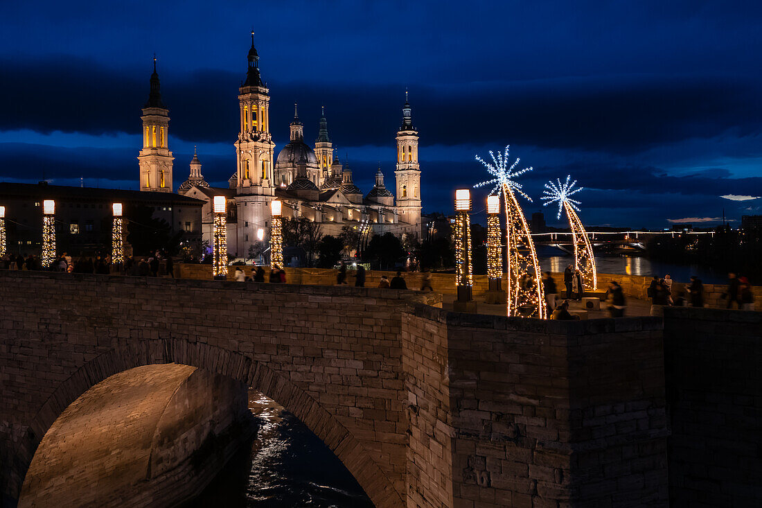 Aerial view of the Cathedral Basilica of Our Lady of the Pillar and Stone Bridge illuminated at night during Christmas, Zaragoza, Spain