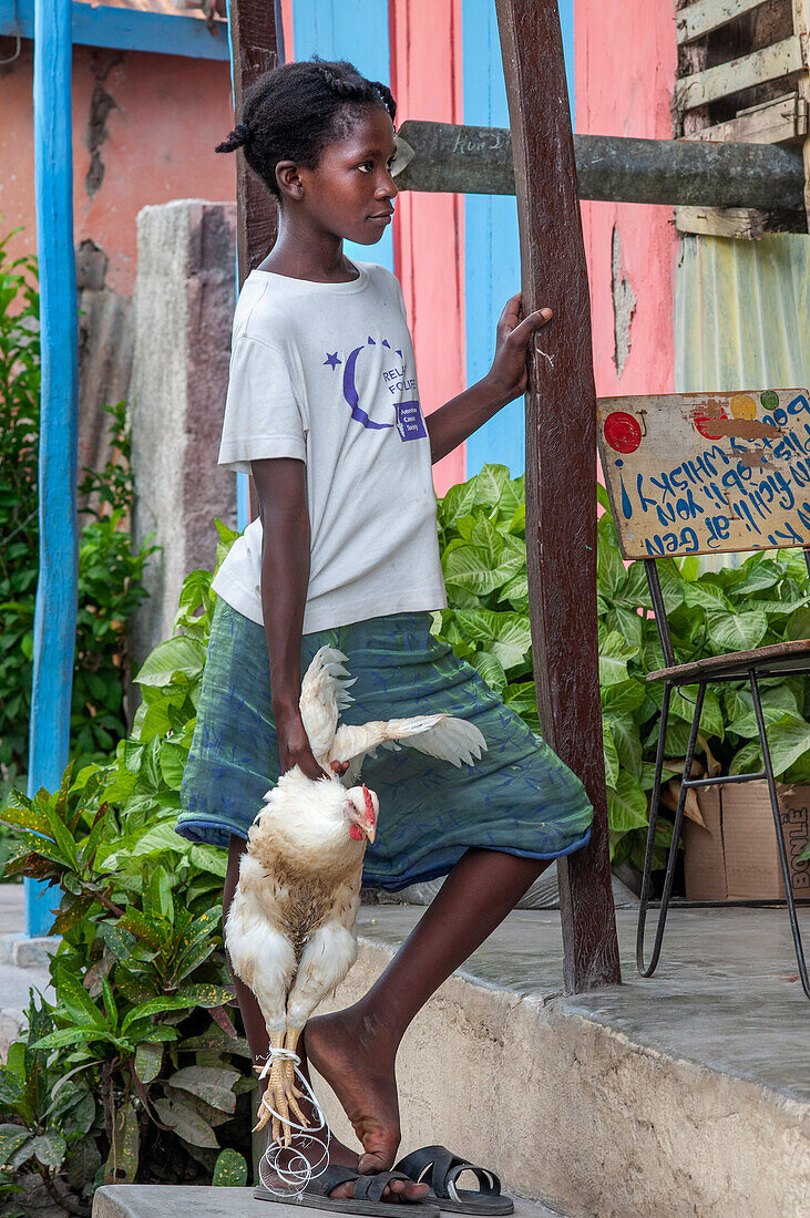 Girl selling a chicken in a local market and houses in the historic colonial old town, Jacmel city center, Haiti, West Indies, Caribbean, Central America