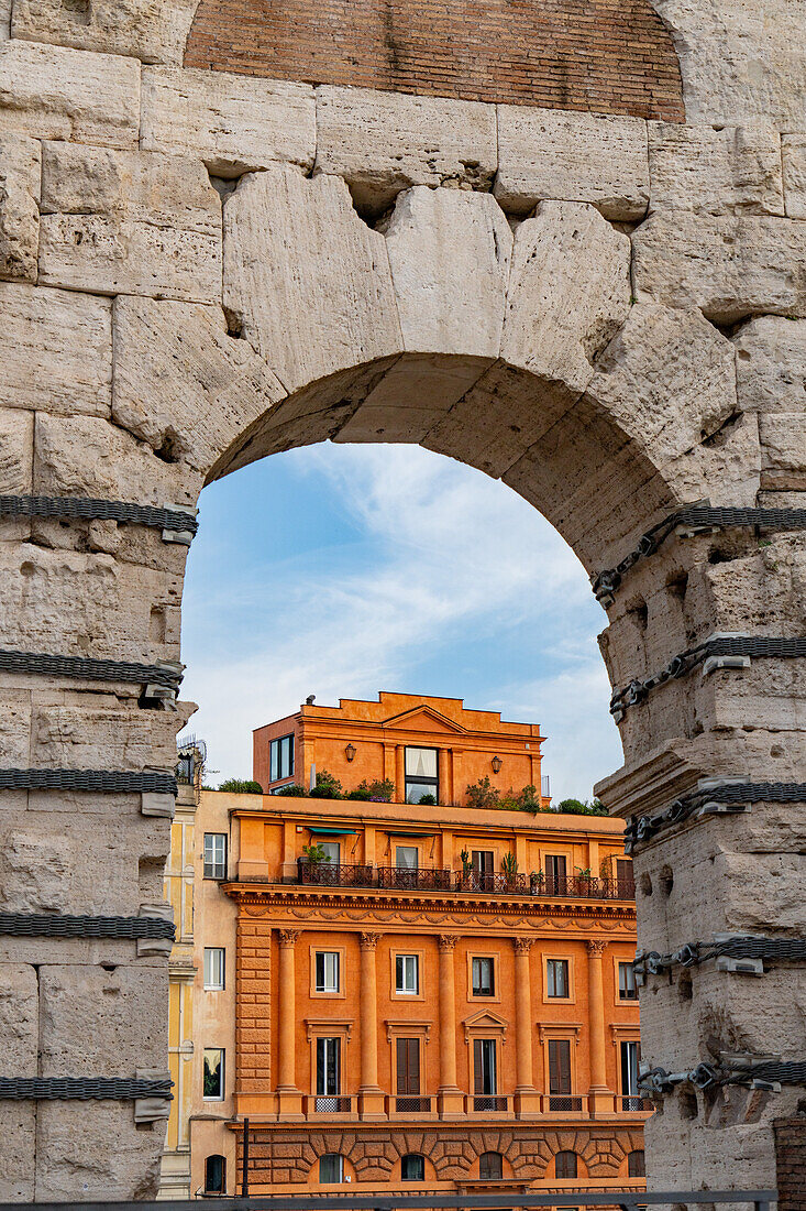 Ein farbenfrohes historisches Luxus-Apartmentgebäude, das durch einen Bogen des Kolosseums in Rom, Italien, betrachtet wird.