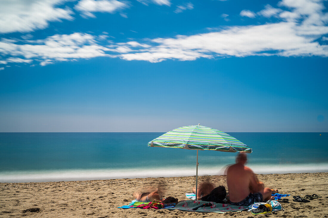 Peaceful beach scene with umbrella and vacationers enjoying sunshine and clear ocean view.