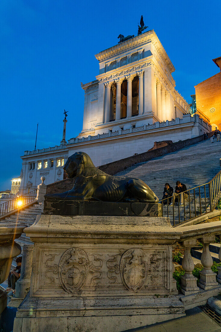 Eine ägyptische Löwenstatue aus Basalt mit dem Denkmal für Viktor Emanuel II. im Hintergrund in Rom, Italien.