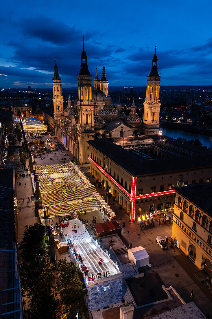 Luftaufnahme der Kathedralenbasilika Unserer Lieben Frau von der Säule und des nachts beleuchteten Platzes El Pilar während der Weihnachtszeit, Zaragoza, Spanien