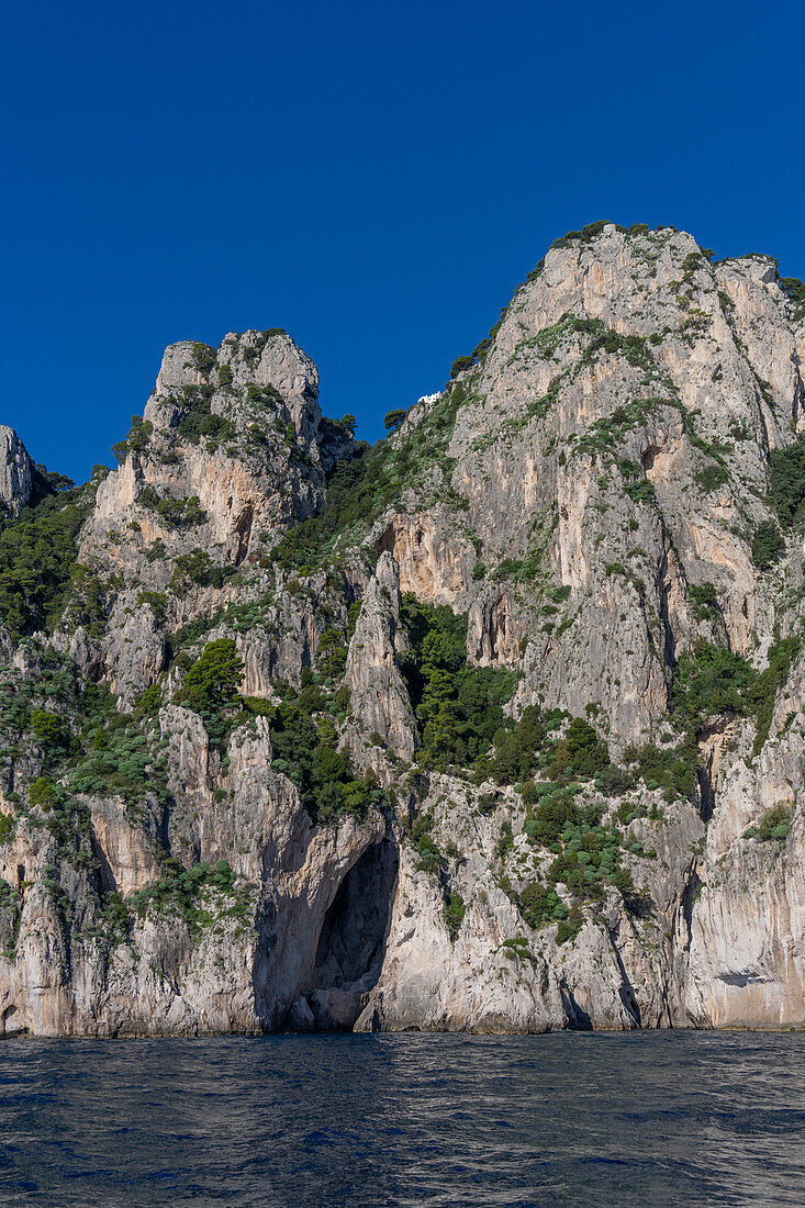 An unnamed grotto in the limestone cliffs of the coast of the island of Capri, Italy. A villa is perched high on the cliff top.