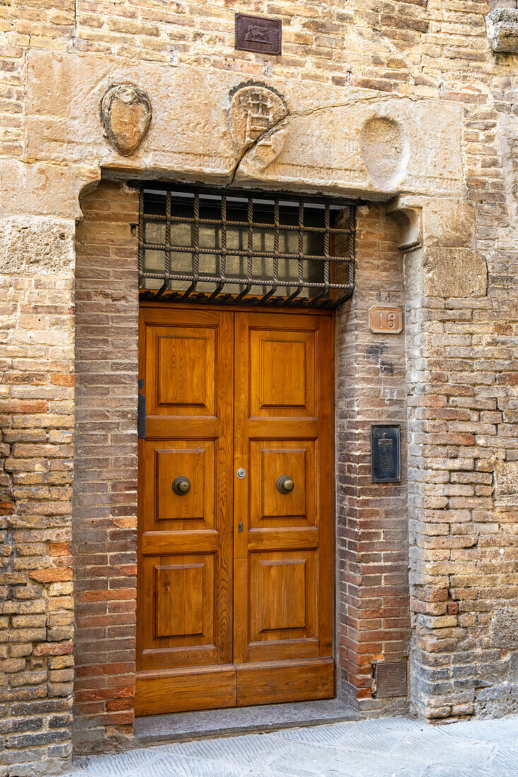 Eine Holztür und alte Steinmetzarbeiten in der Via San Giovanni in der ummauerten Stadt San Gimignano, Italien.