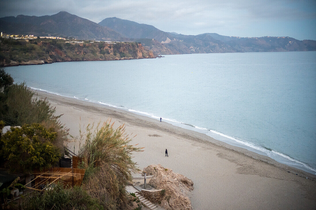 A serene beach with calm waters, distant mountains, and coastal beauty at dusk.