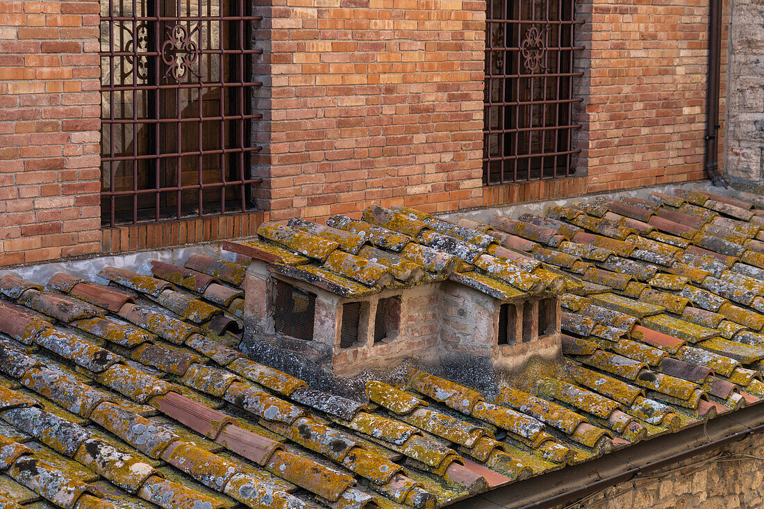 A traditional chimney & lichen-covered roof tiles on a building in the medieval walled town of San Gimignano, Italy.