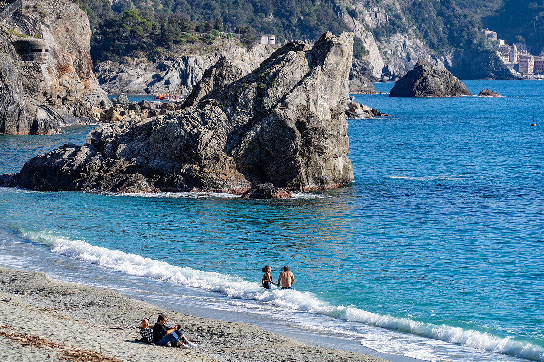 Touristen am Strand außerhalb der Hauptsaison in Monterosso al Mare, Cinque Terre, Italien. Dahinter befindet sich der Malpasso-Felsen.