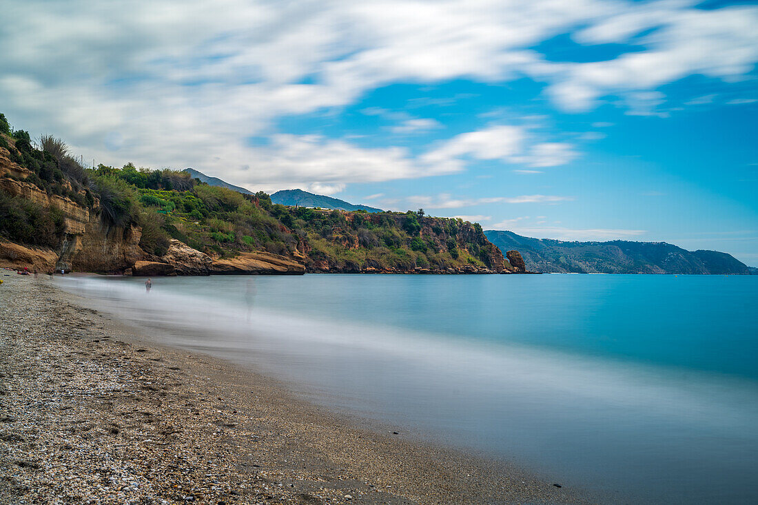 Long exposure photograph of Burriana Beach with Maro Cliffs and serene blue waters.