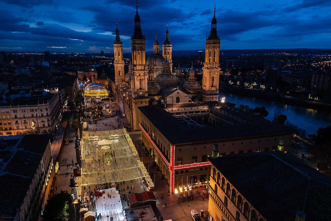 Luftaufnahme der Kathedralenbasilika Unserer Lieben Frau von der Säule und des nachts beleuchteten Platzes El Pilar während der Weihnachtszeit, Zaragoza, Spanien