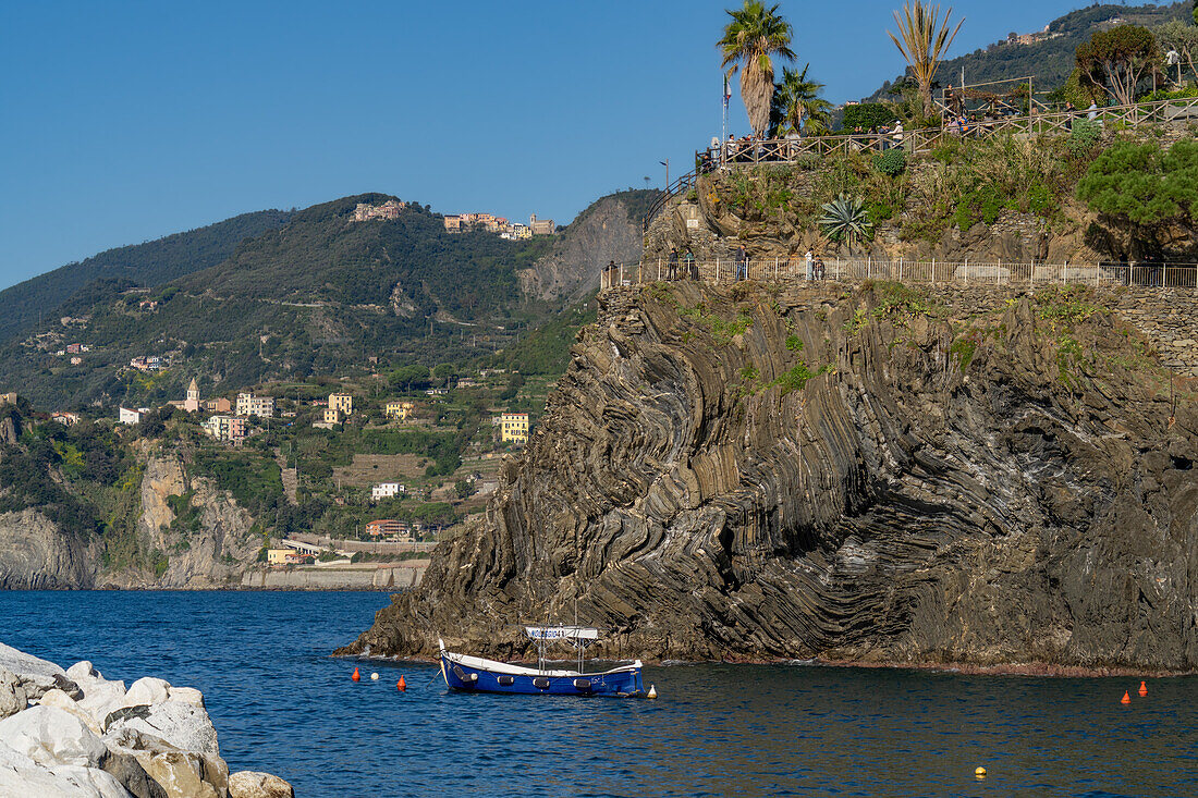 Ein kleines Fischerboot liegt im kleinen Hafen des Fischerdorfs Manarola in den Cinque Terre, Italien. Dahinter liegt das Dorf Corniglia.