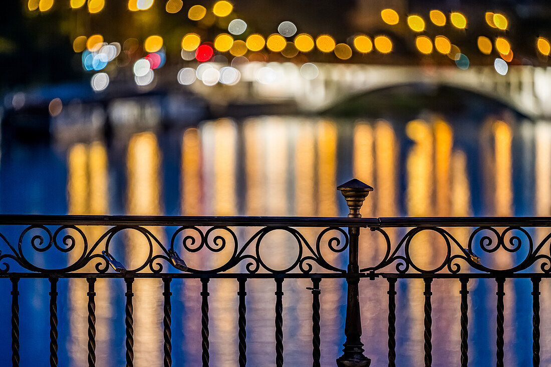 Intricate ironwork balustrade of Triana Bridge with colorful light reflections in a serene nighttime setting.