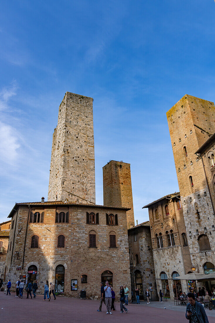 Touristen auf der Piazza del Duomo mit ihren Türmen in der mittelalterlichen Festungsstadt San Gimignano, Italien. L-R: Torri Salvucci und Torre Pettini.