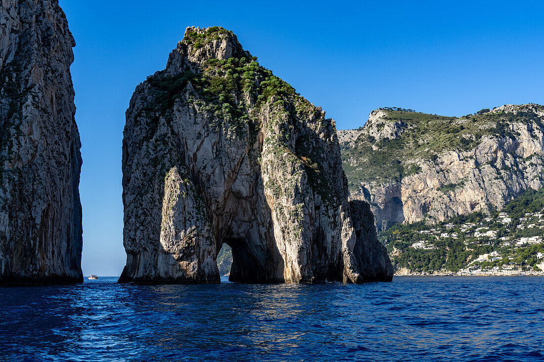 The Farallons or faraglioni, sea stacks off the coast of the island of Capri, Italy. L-R: Scopolo or Fuori & Mezzo with its sea arch. A boat is visible between. At right is the town of Marina Piccola.