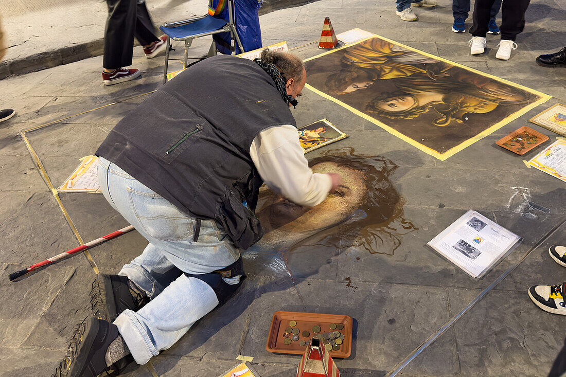 An artist reproduces classic paintings with chalk on the flagstones of a street in Florence, Italy, working only for tips. The drawings are cleaned off the street every night.