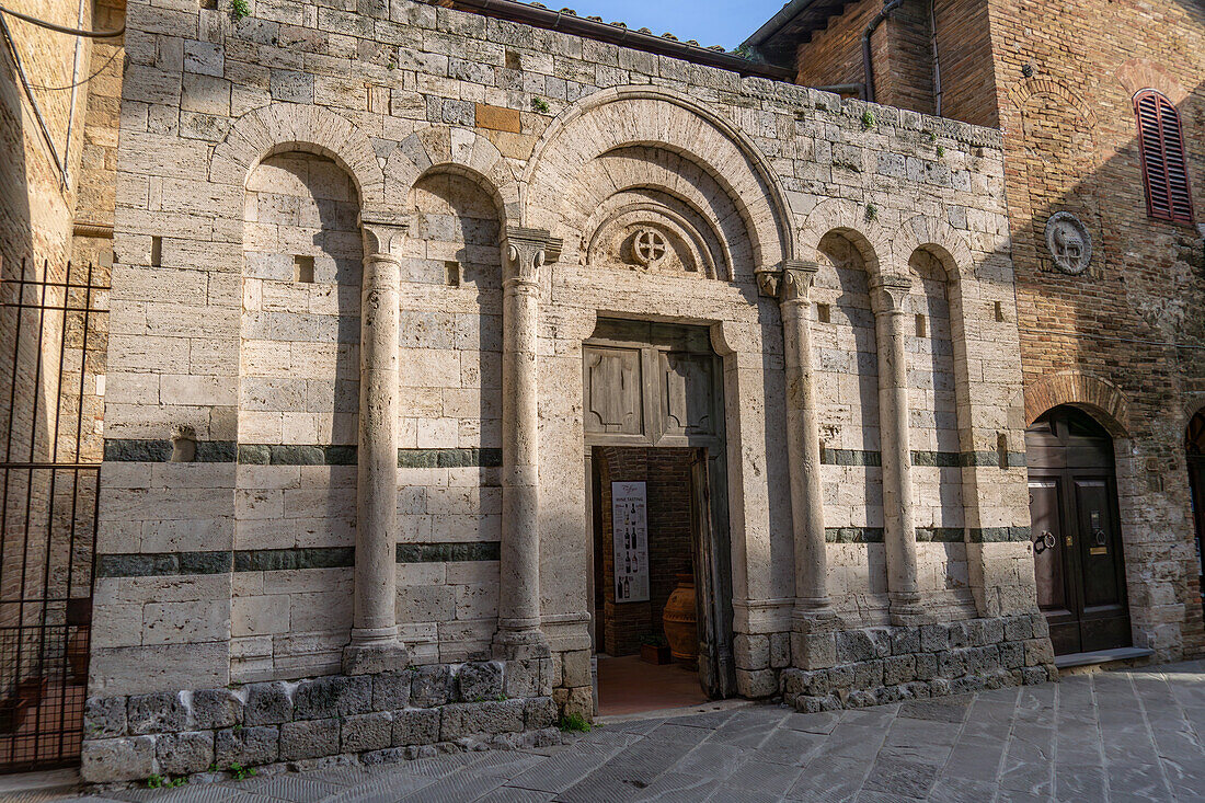 The facade of the ruins of the Church of St. Francis in the medieval walled city of San Gimignano, Italy. At right is the Agnus Dei symbol of the medieval wool Guild.