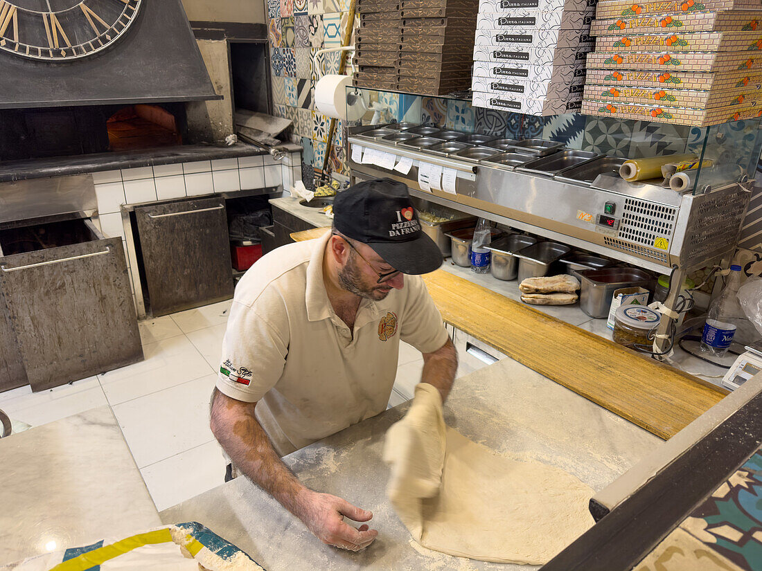 Ein Pizzaiolo oder Pizzabäcker bereitet den Teig für eine Pizza in einer Pizzeria in Sorrento, Italien, vor.