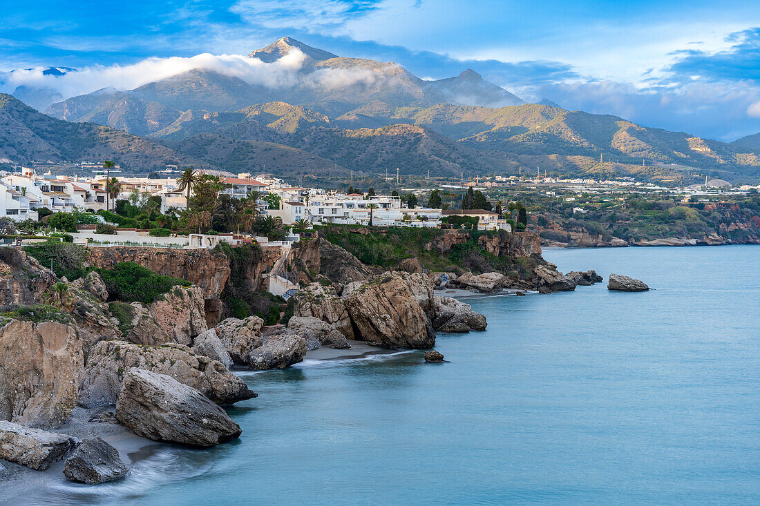 Wunderschöne Küstenlandschaft mit Klippen, ruhigem Meer und bergiger Kulisse in Nerja, Spanien.