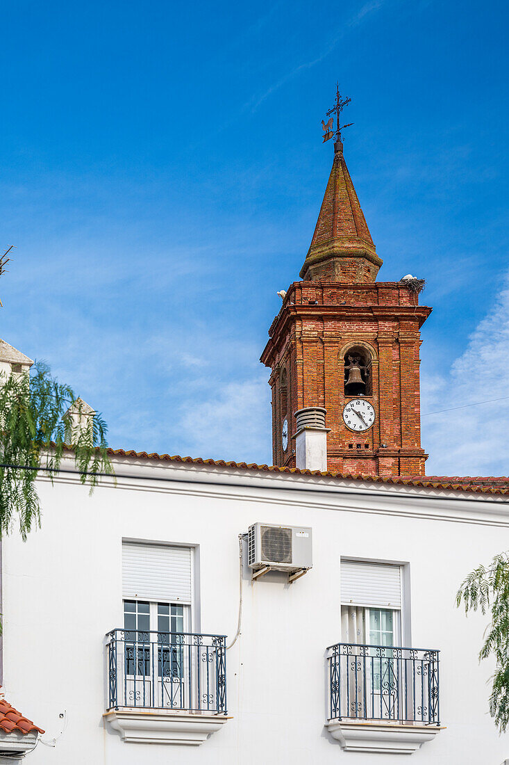 Old brick bell tower with clock and white architecture under a clear sky