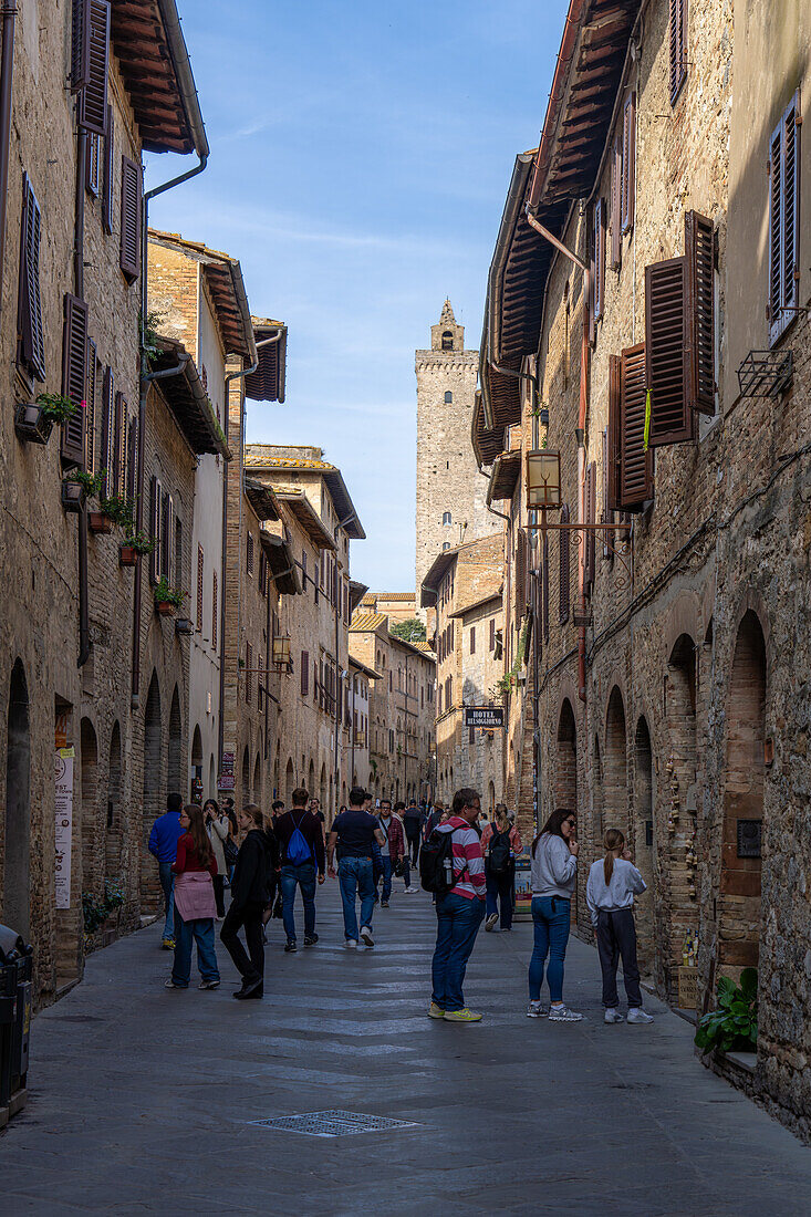 Touristen auf der Via San Gimignano in der mittelalterlichen Stadt San Gimignano, Italien. Dahinter befindet sich der Torre Grossa.