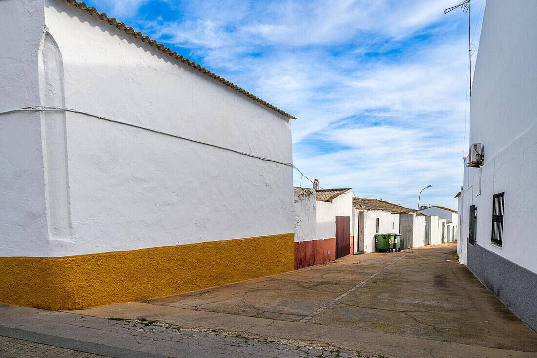 A narrow street lined with traditional whitewashed houses under a bright blue sky.