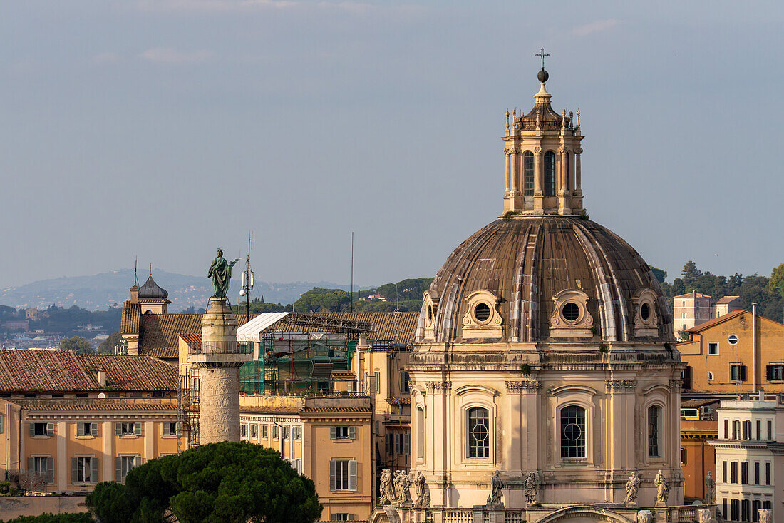 Kuppel der Kirche des Allerheiligsten Namen Mariens am Trajansforum in Rom, Italien. Links ist die Trajanssäule zu sehen, die von einer Statue des Heiligen Petrus gekrönt wird.