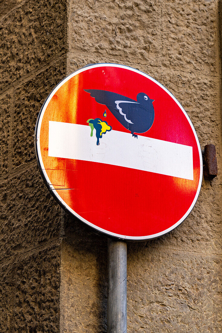 Humorvolle Darstellung eines Vogels, der auf ein Straßenschild in Florenz, Italien, kackt.