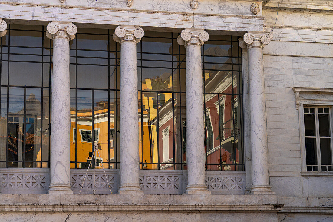 Colorful buildings are reflected in the glass of the Animosi Theater on Piazza Fabrizio de Andre in Carrara, Italy.