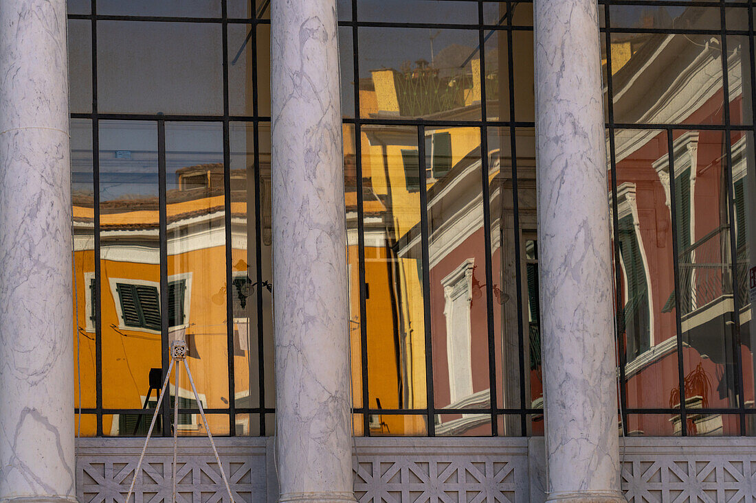 Colorful buildings are reflected in the glass of the Animosi Theater on Piazza Fabrizio de Andre in Carrara, Italy.