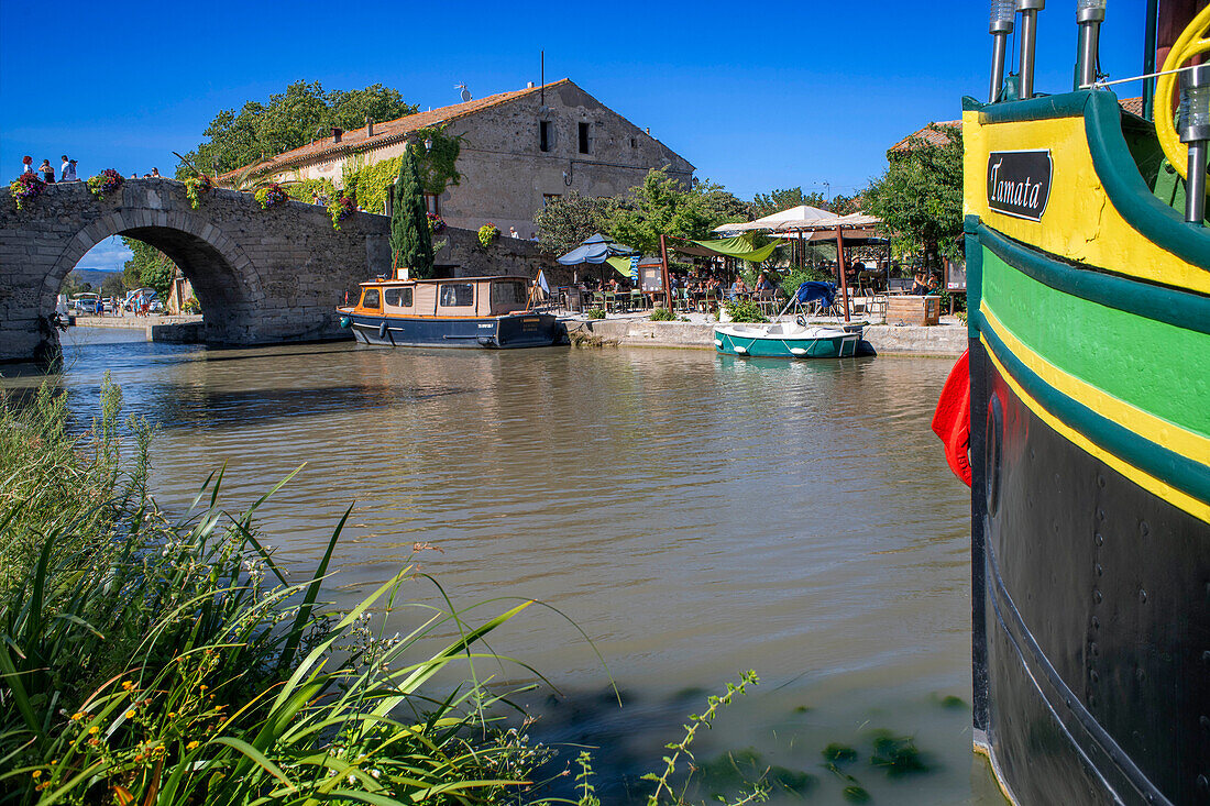 Canal du Midi an Brücke und Dorf Le Somail Aude Südfrankreich Südliche Wasserstraße Wasserstraßen Urlauber stehen Schlange für eine Bootsfahrt auf dem Fluss, Frankreich, Europa