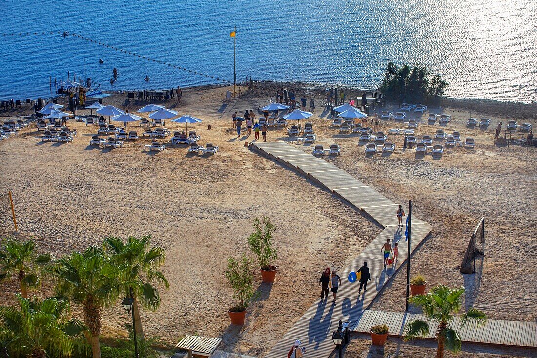 Menschen schwimmen und sind mit schwarzem Schlamm aus dem Toten Meer bedeckt, am Strand des Crowne Plaza Dead Sea Hotels am Toten Meer, Jordanien.