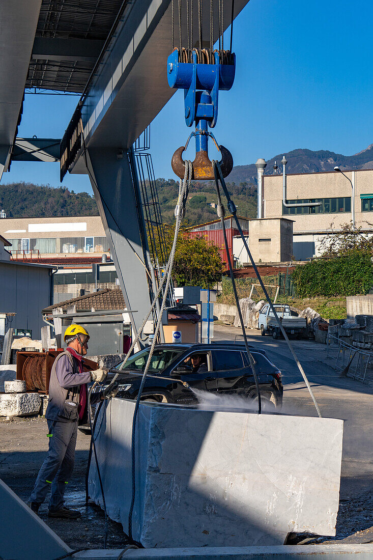 A worker powerwashes a large block of marble at a marble supply company yard in Carrara, Italy.