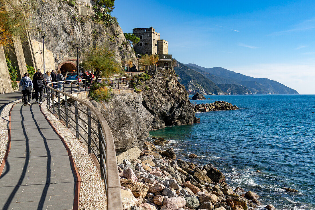 Touristen auf der Promenade mit dem Aurora-Turm im Hintergrund. Monterosso al Mare, Cinque Terre, Italien.