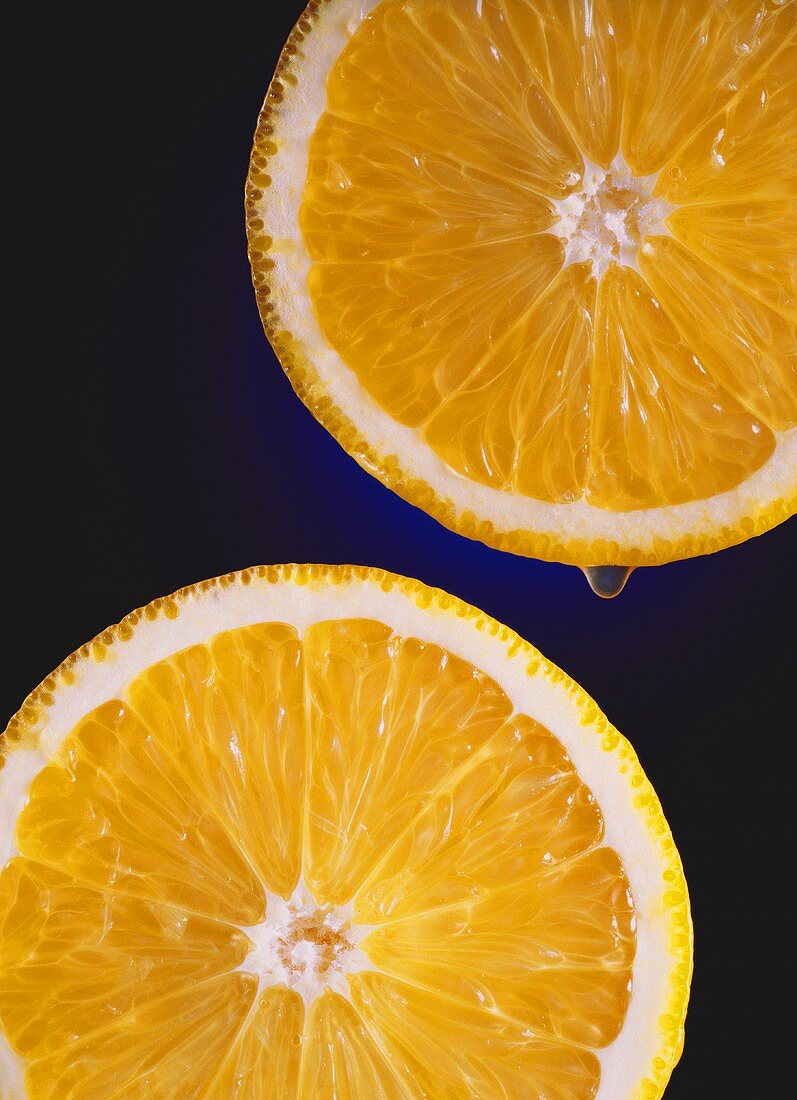 Zwei Orangenscheiben, eine mit Tropfen, auf blauem Untergrund