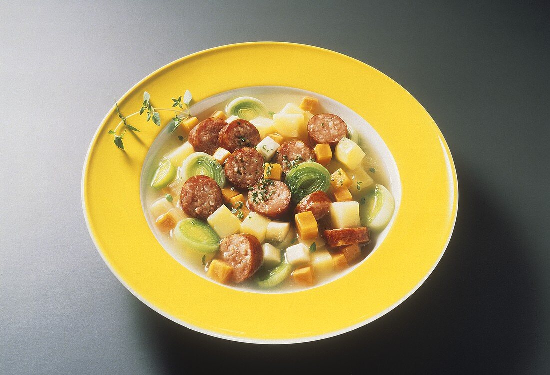 Vegetable stew with sausage slices on yellow plate
