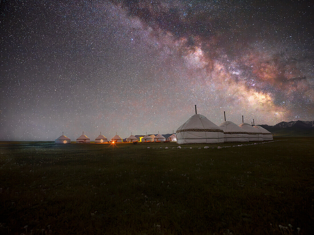 A row of white yurts illuminated by the Milky Way, stretching across the night sky, Song Kol Lake area, Kyrgyzstan