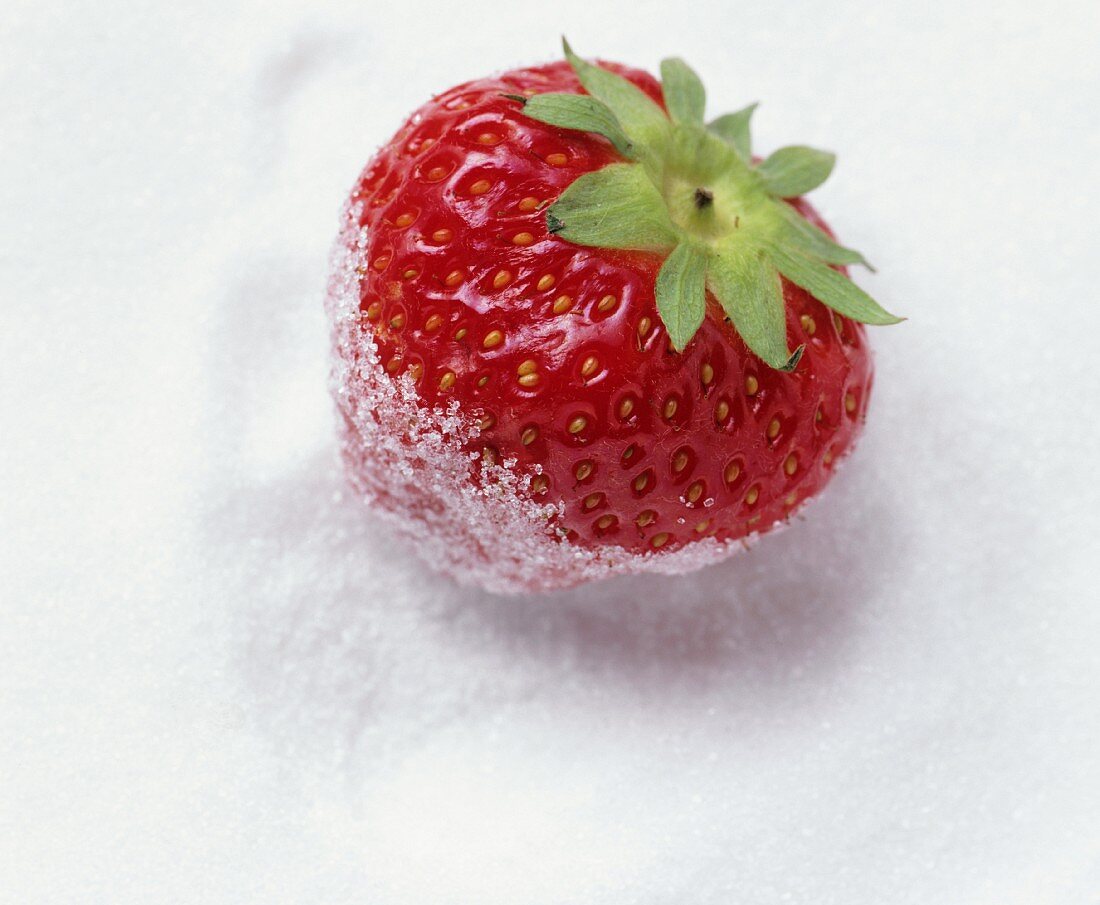 Eine Erdbeere liegt auf Kristallzucker