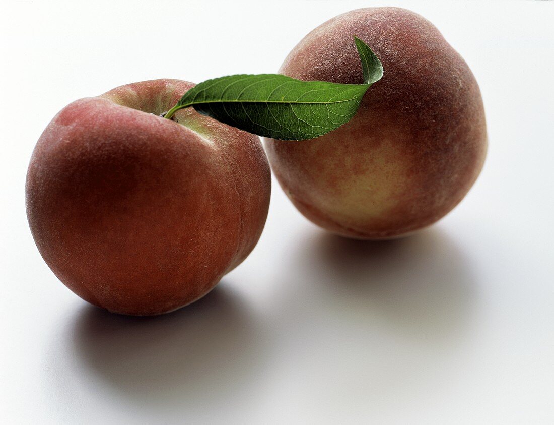 Zwei Pfirsiche, einer davon mit Blatt
